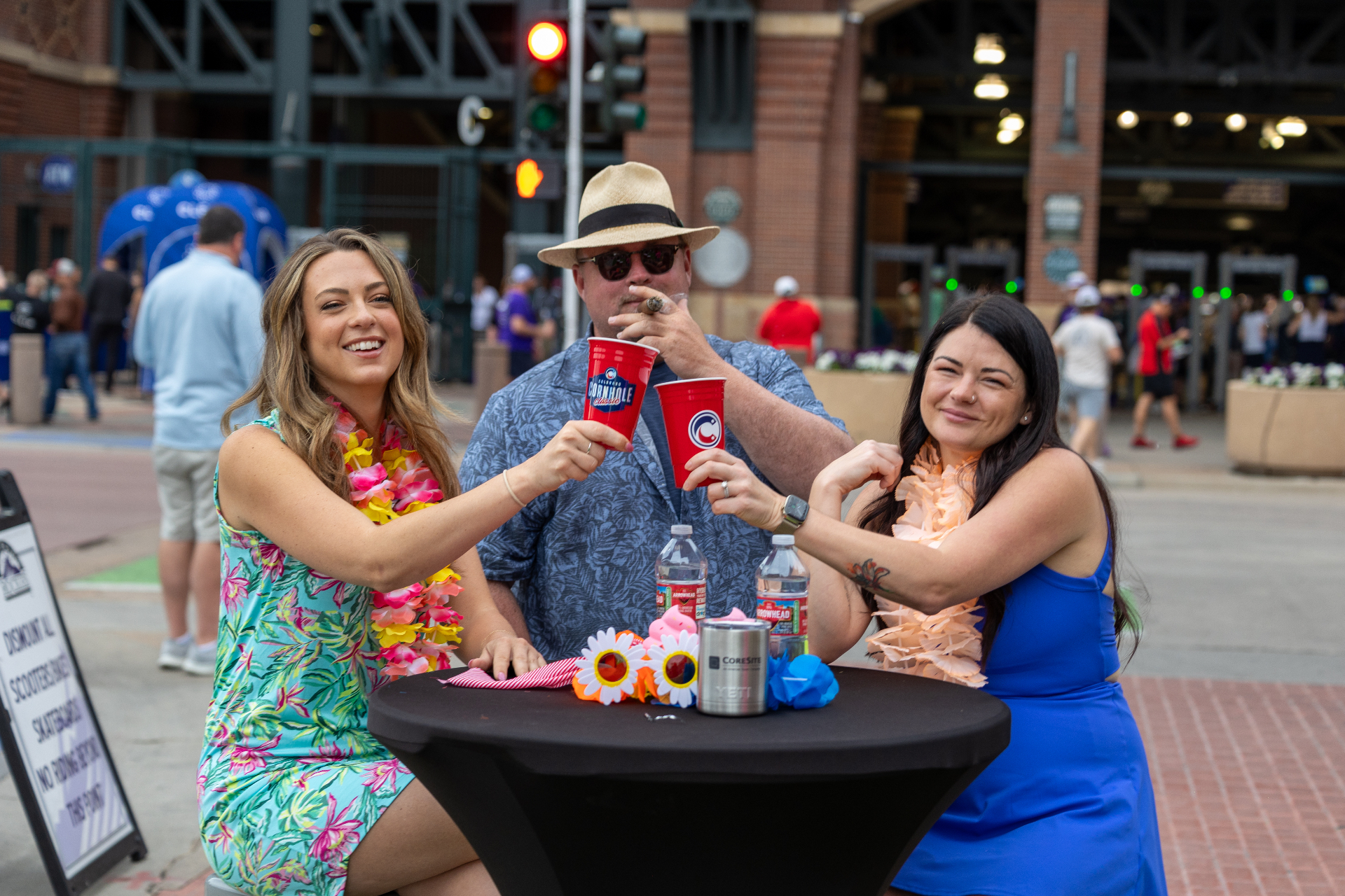 Three people toasting at a table outside Coors Field during the Colorado Cornhole Classic